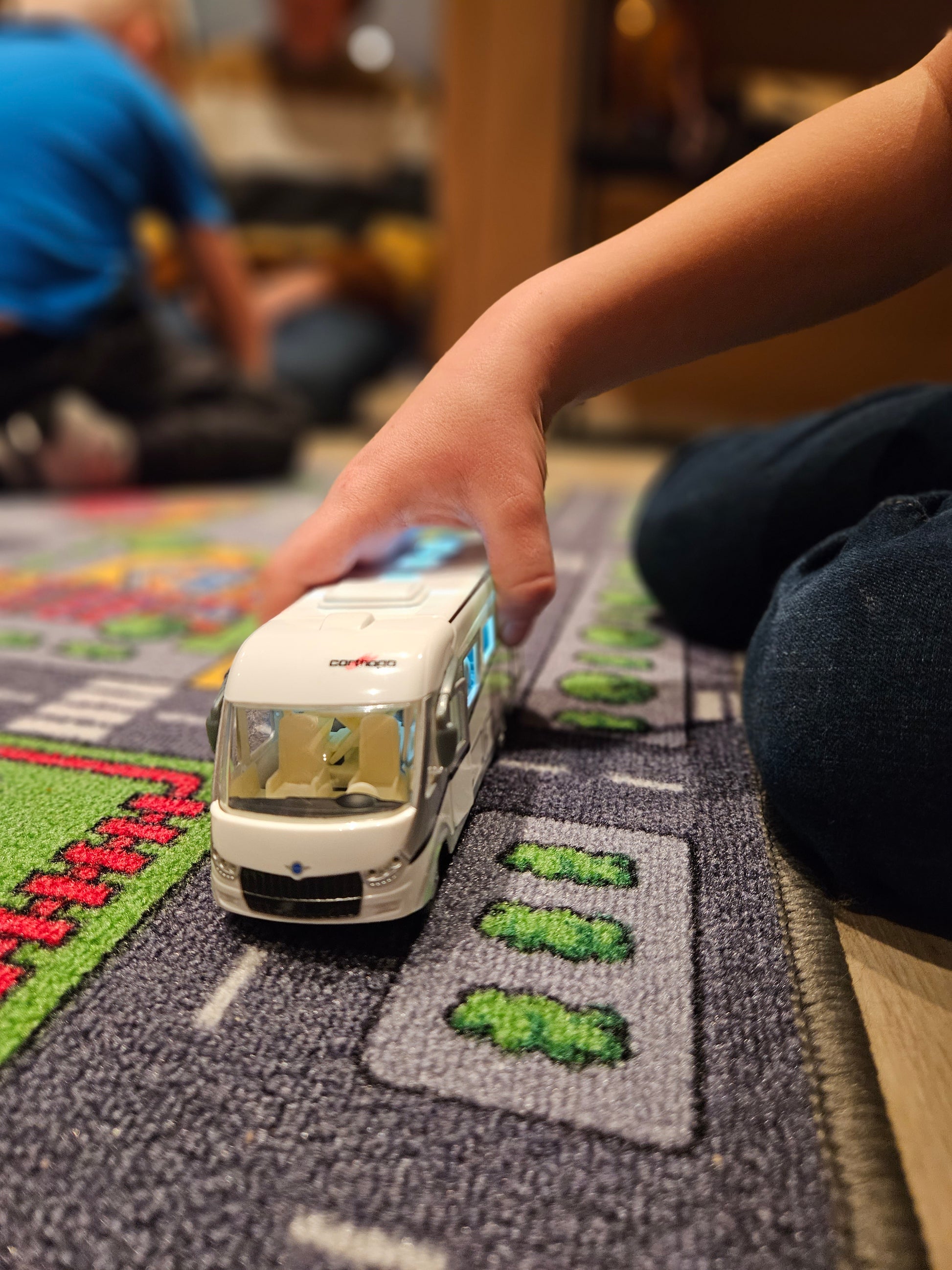 2 barn leker med bobil og andre biler på et lekebilteppe