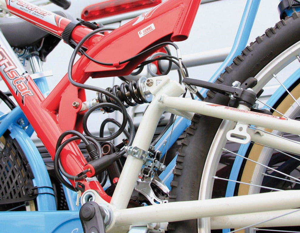 2 sykler med rød og blå ramme låst med sykkellås til et sykkelstativ på en bobil